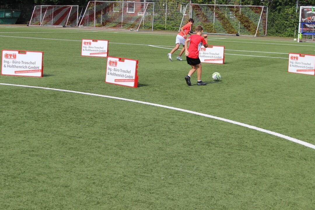 Zwei Kinder spielen Fu&szlig;ball auf einem Kunstrasenplatz, umgeben von Werbeschildern.