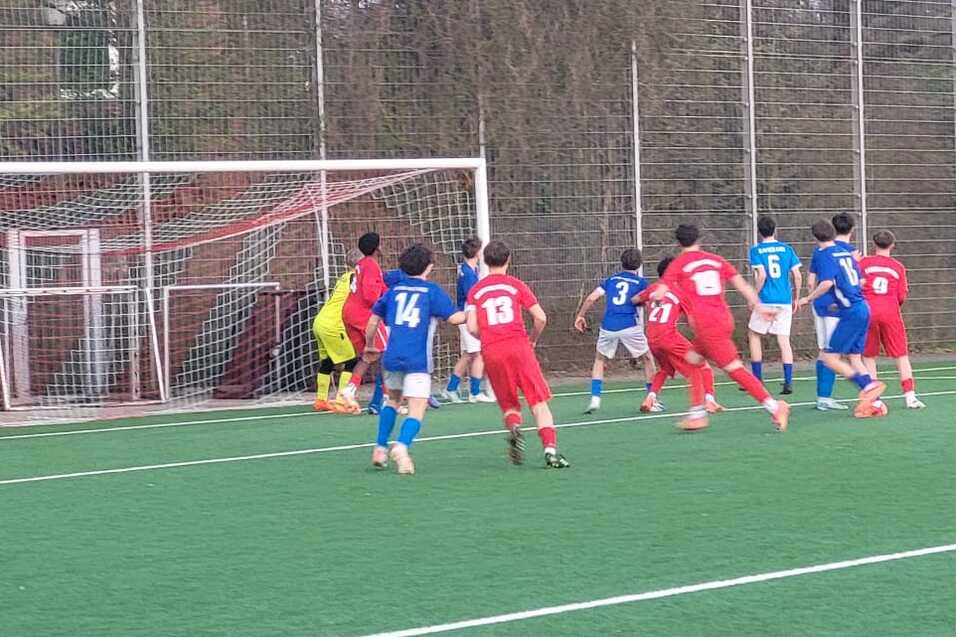 Spielszene auf einem Fu&szlig;ballplatz: Spieler in blauen und roten Trikots warten auf einen Freisto&szlig; in der N&auml;he des Tors.