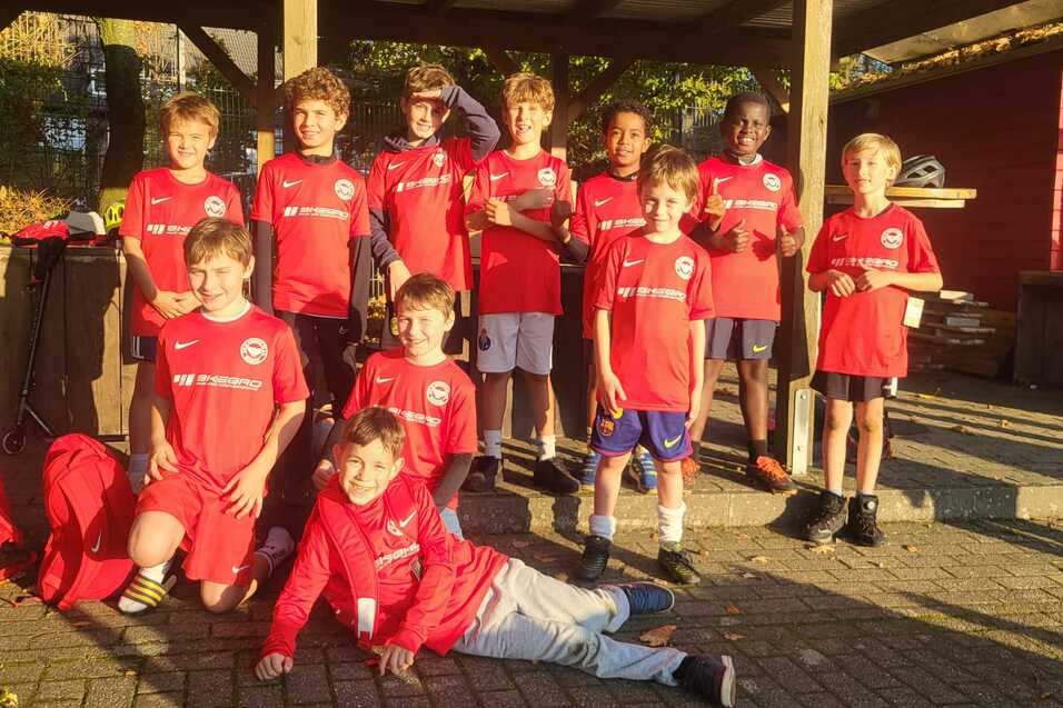 Gruppe von zehn Kindern in roten Fu&szlig;balltrikots, l&auml;chelnd, im Freien unter einem Pavillon.