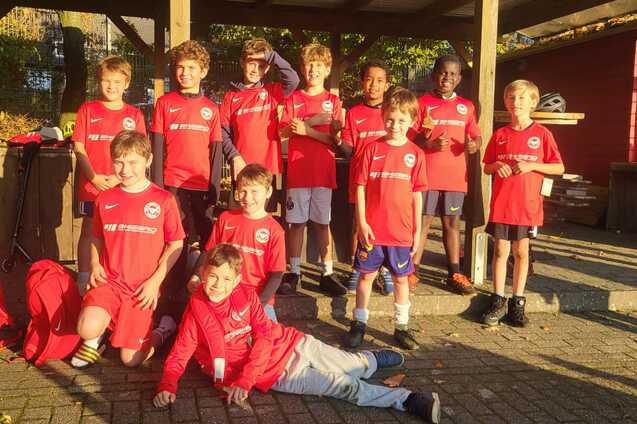 Gruppe von zehn Kindern in roten Fu&szlig;balltrikots, l&auml;chelnd, im Freien unter einem Pavillon.