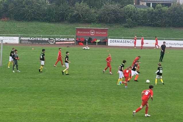 Jugendfu&szlig;ballspiel auf gr&uuml;nem Rasen mit Spielern in roten und schwarzen Trikots sowie einem Tor im Hintergrund.