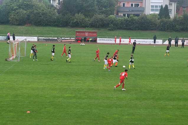 Jugendfu&szlig;ballspiel auf gr&uuml;nem Rasen mit Spielern in roten und schwarzen Trikots sowie einem Tor im Hintergrund.