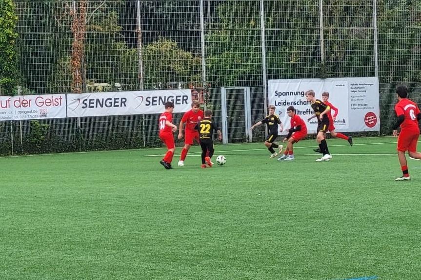 Zwei Jugendfu&szlig;ballmannschaften spielen auf einem Kunstrasenplatz, w&auml;hrend ein Spieler mit der Nummer 22 den Ball f&uuml;hrt.