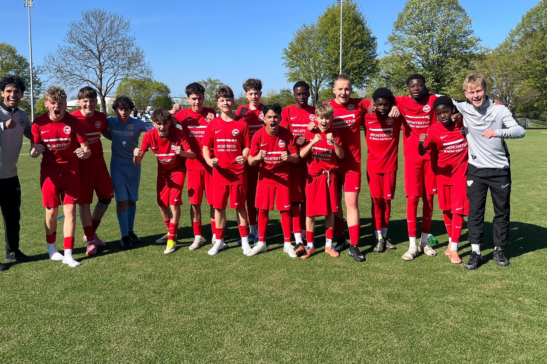 Gruppe junger Fu&szlig;ballspieler in roten Trikots posiert auf einem gr&uuml;nen Feld unter blauem Himmel.