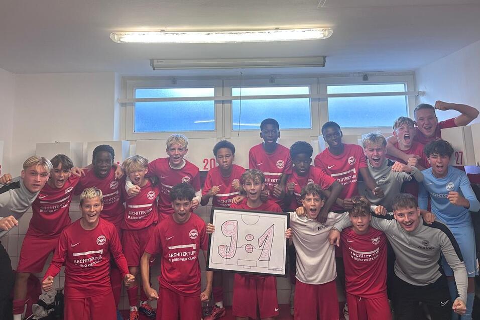 Gruppenselfie von Jugendfu&szlig;ballspielern in roten Trikots, die jubilieren und ein 9:1-Schild halten.