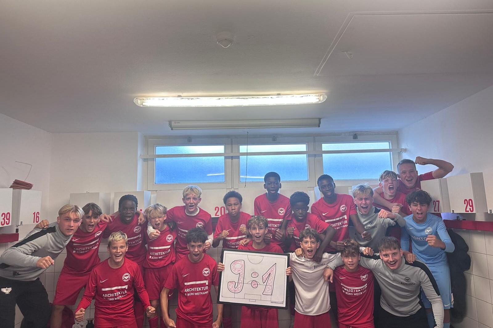 Gruppenselfie von Jugendfu&szlig;ballspielern in roten Trikots, die jubilieren und ein 9:1-Schild halten.