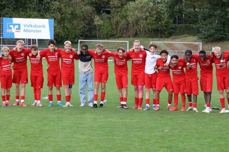 Gruppensportmannschaft in roten Trikots posiert gemeinsam auf einem Fu&szlig;ballplatz.