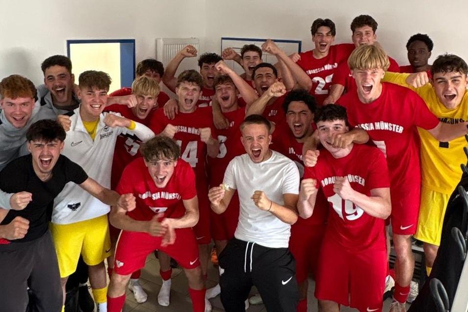 Gruppe von jubelnden Fu&szlig;ballspielern in roten Trikots vor einer Umkleidekabine, die ihren Sieg feiern.