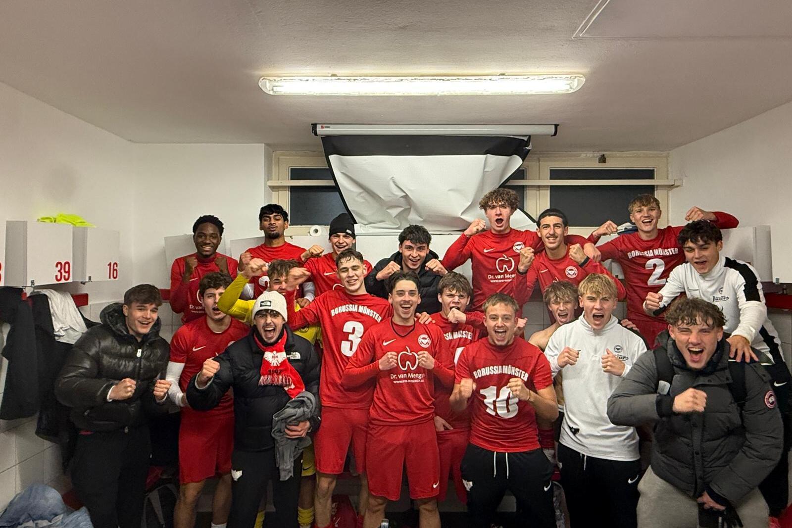 Gruppe junger Fu&szlig;ballspieler in roten Trikots feiert fr&ouml;hlich in einer Umkleidekabine.