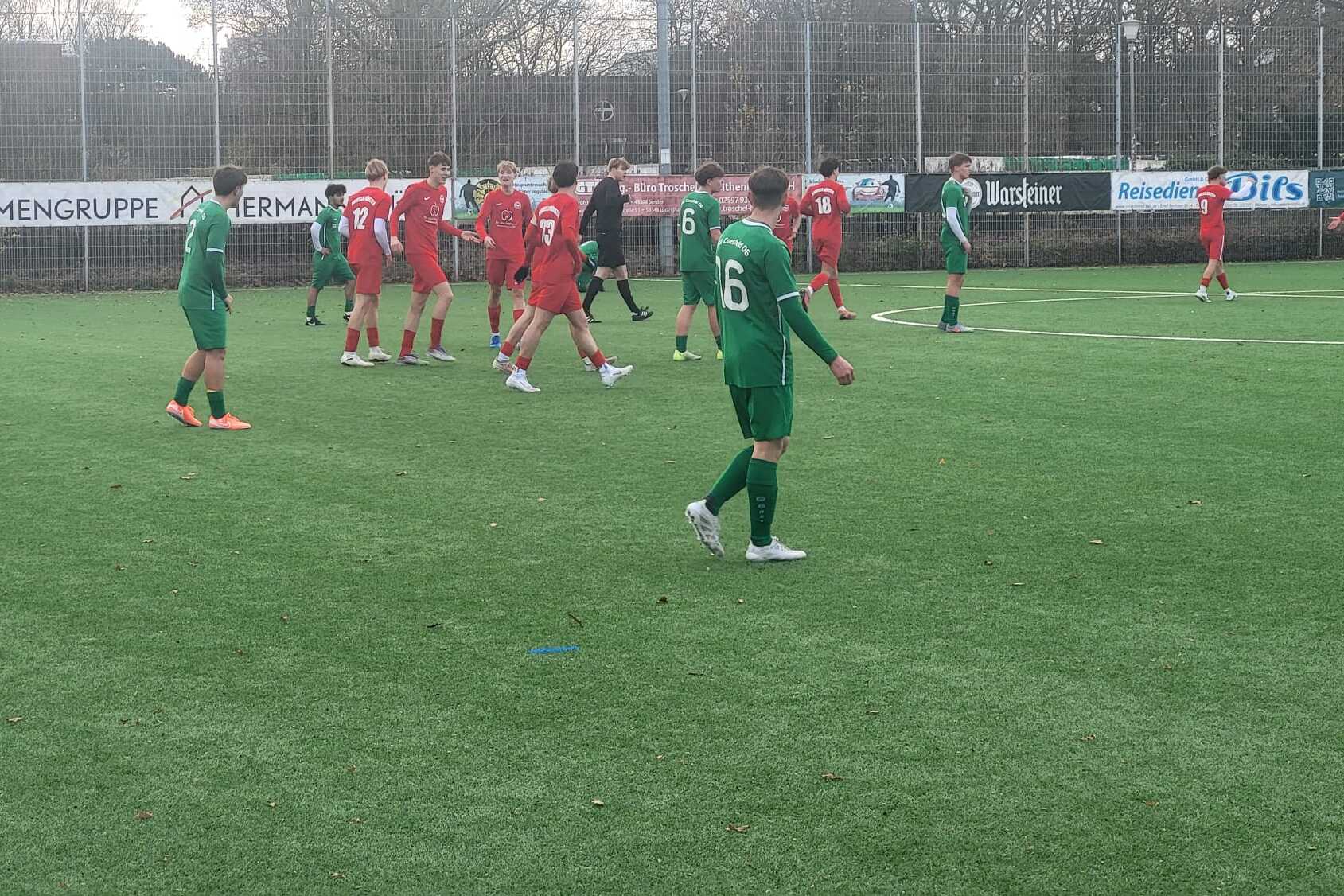 Fu&szlig;ballspiel auf einem Kunstrasenplatz mit Spielern in gr&uuml;nen und roten Trikots in Aktion.