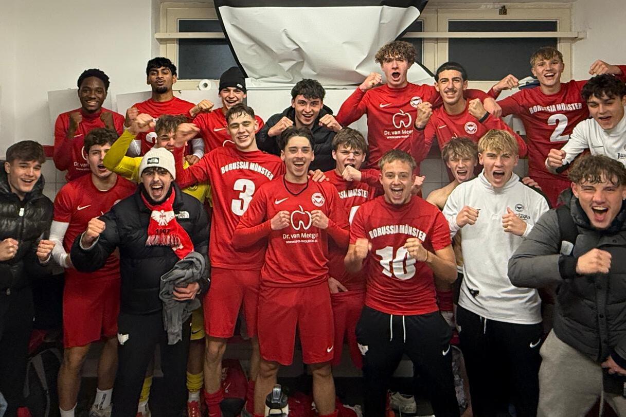 Gruppe junger Fußballspieler in roten Trikots feiert fröhlich in einer Umkleidekabine.