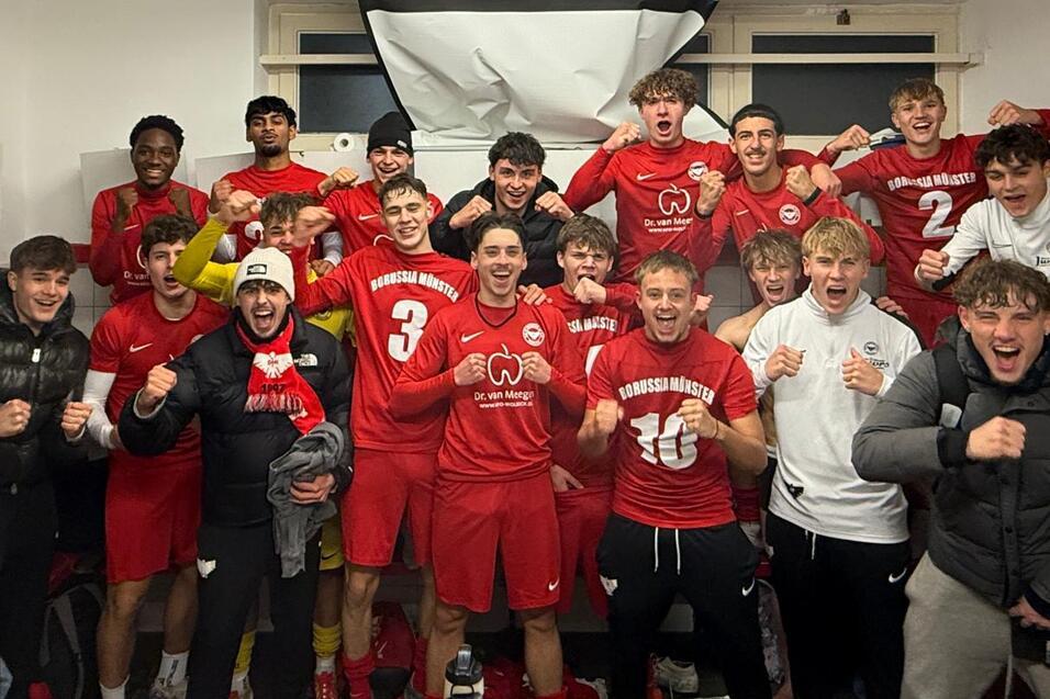 Gruppe junger Fu&szlig;ballspieler in roten Trikots feiert fr&ouml;hlich in einer Umkleidekabine.