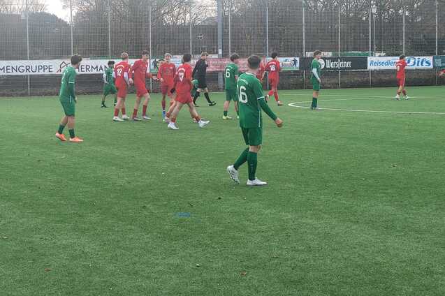Fu&szlig;ballspiel auf einem Kunstrasenplatz mit Spielern in gr&uuml;nen und roten Trikots in Aktion.