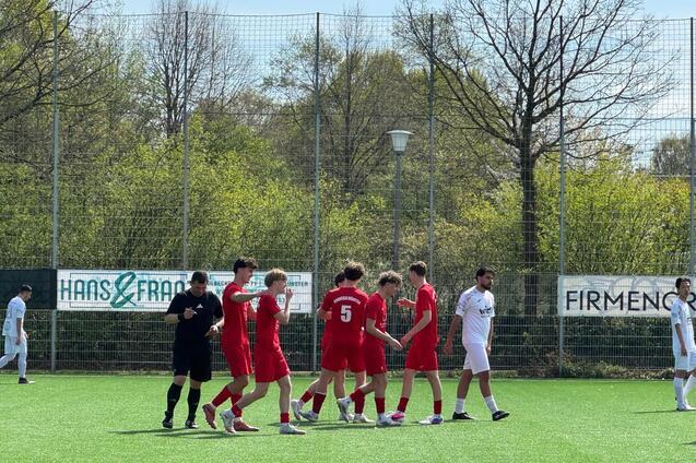Sechs Fu&szlig;ballspieler in roten Trikots stehen auf einem Kunstrasenplatz, w&auml;hrend ein Schiedsrichter in Schwarz daneben steht.