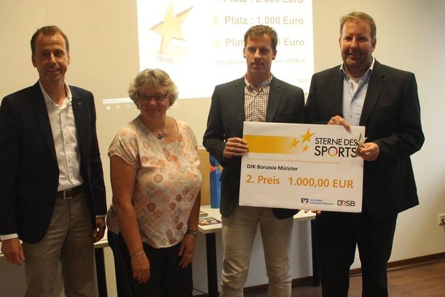 Vier Personen stehen in einem Raum und halten ein gro&szlig;es Preis-Zertifikat f&uuml;r den zweiten Platz beim Wettbewerb &bdquo;Sterne des Sports&ldquo;.