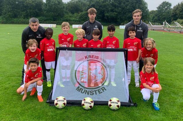 Gruppe von Fu&szlig;ballspielern in roten Trikots posiert vor einem Banner mit dem Schriftzug &bdquo;KREIS M&Uuml;NSTER&ldquo; auf einem Rasenplatz.