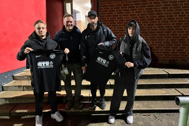 Vier Personen stehen auf einer Treppe vor einem roten Hintergrund und halten schwarze T-Shirts mit dem Aufdruck &bdquo;CTU&ldquo; in der Hand.