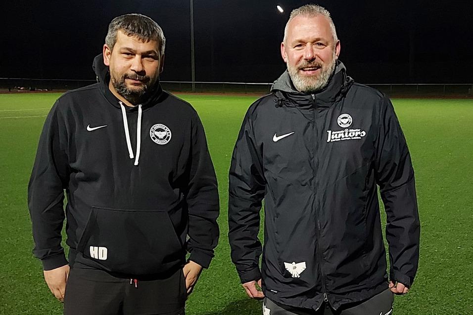 Zwei Trainer stehen auf einem beleuchteten, gr&uuml;nen Fu&szlig;ballfeld in der Dunkelheit.
