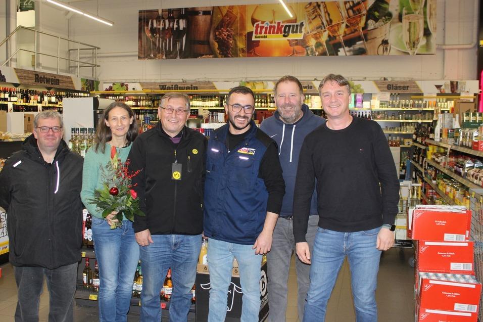 Gruppe von sechs Personen im Getr&auml;nkemarkt, umgeben von Regalen mit verschiedenen Getr&auml;nken.