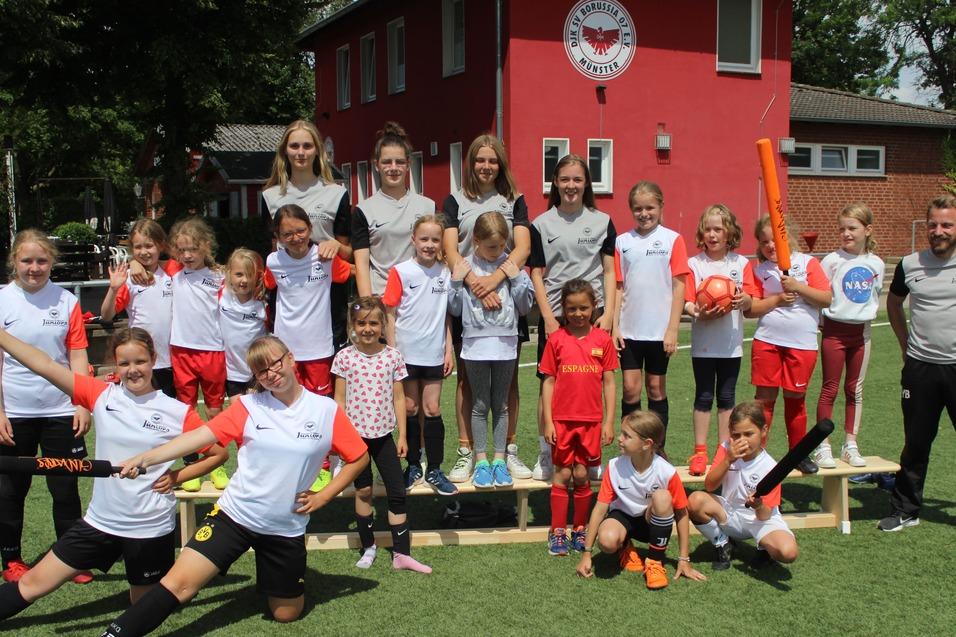Gruppe von Fu&szlig;ballspielerinnen und -spielern auf einem Sportplatz, einige halten orangefarbene Sportger&auml;te.
