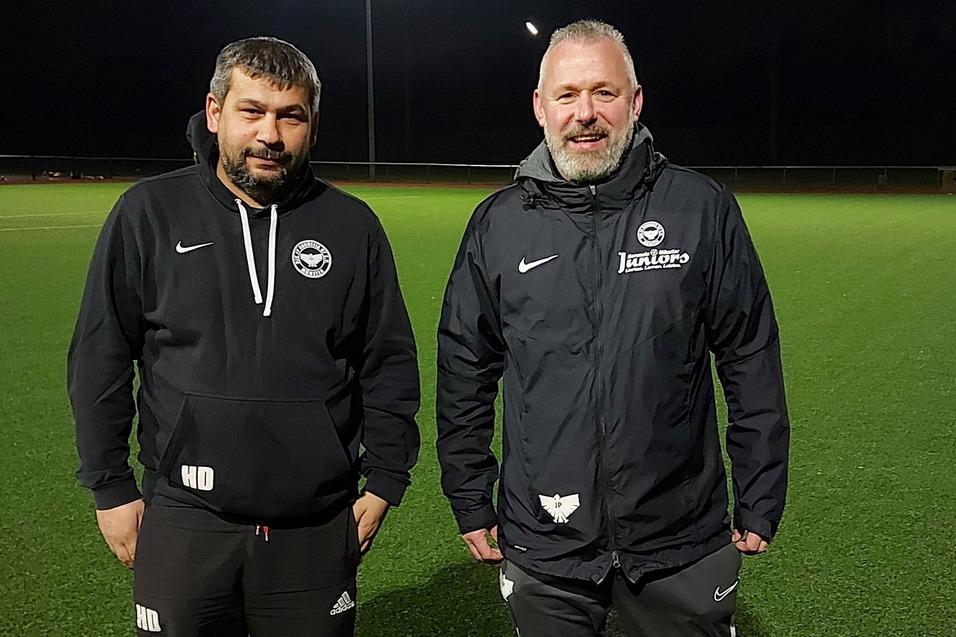 Zwei Trainer stehen auf einem beleuchteten, gr&uuml;nen Fu&szlig;ballfeld in der Dunkelheit.