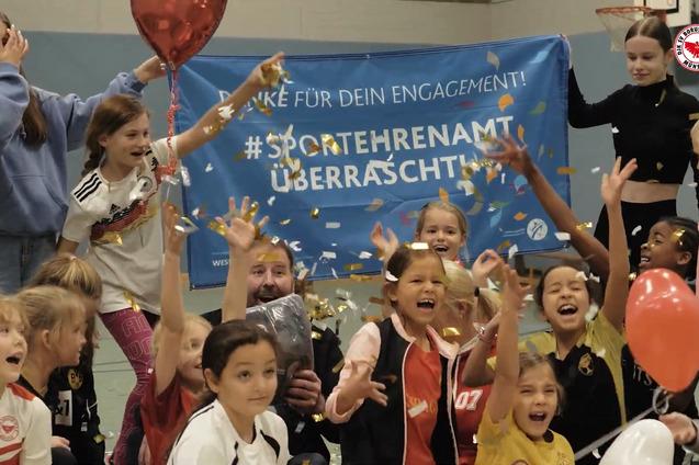 Gruppenfoto von l&auml;chelnden Kindern und Jugendarbeitern, umgeben von Luftballons und Konfetti, vor einem Banner &uuml;ber Ehrenamt.