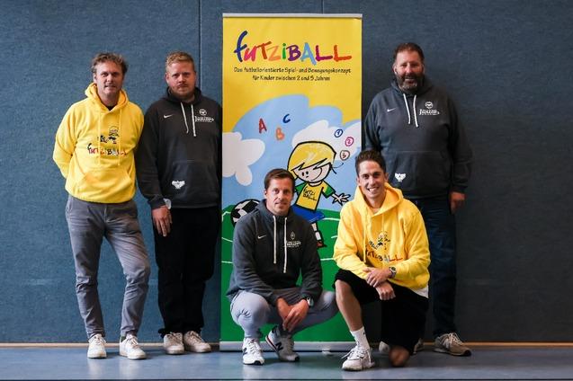 F&uuml;nf M&auml;nner in Sportswear stehen vor einem Banner mit der Aufschrift &bdquo;FurtziBALL&ldquo; und einem Kindermotiv.