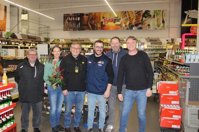 Gruppe von sechs Personen im Getr&auml;nkemarkt, umgeben von Regalen mit verschiedenen Getr&auml;nken.