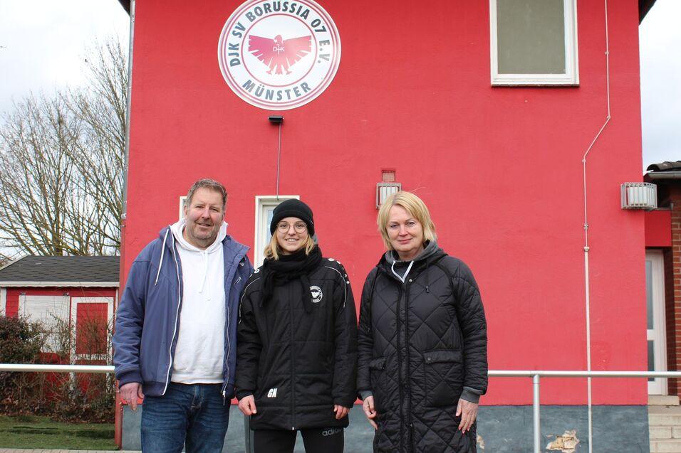 Drei Personen stehen vor einem roten Vereinsgeb&auml;ude mit dem Logo von Borussia M&uuml;nster.