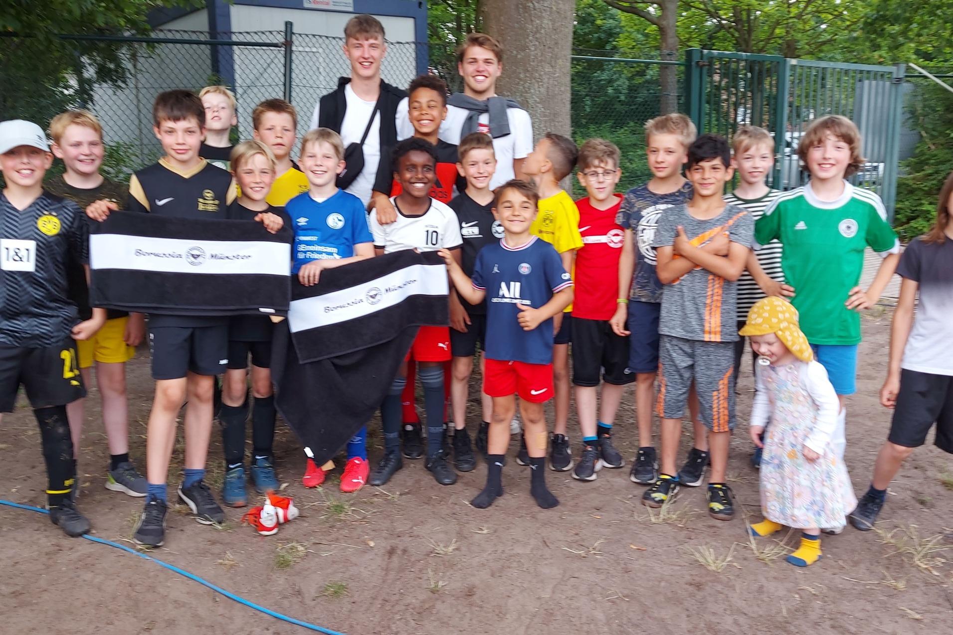 Gruppe von 18 Jungen in Fu&szlig;ballkleidung posiert zusammen im Freien, einige halten Banner.