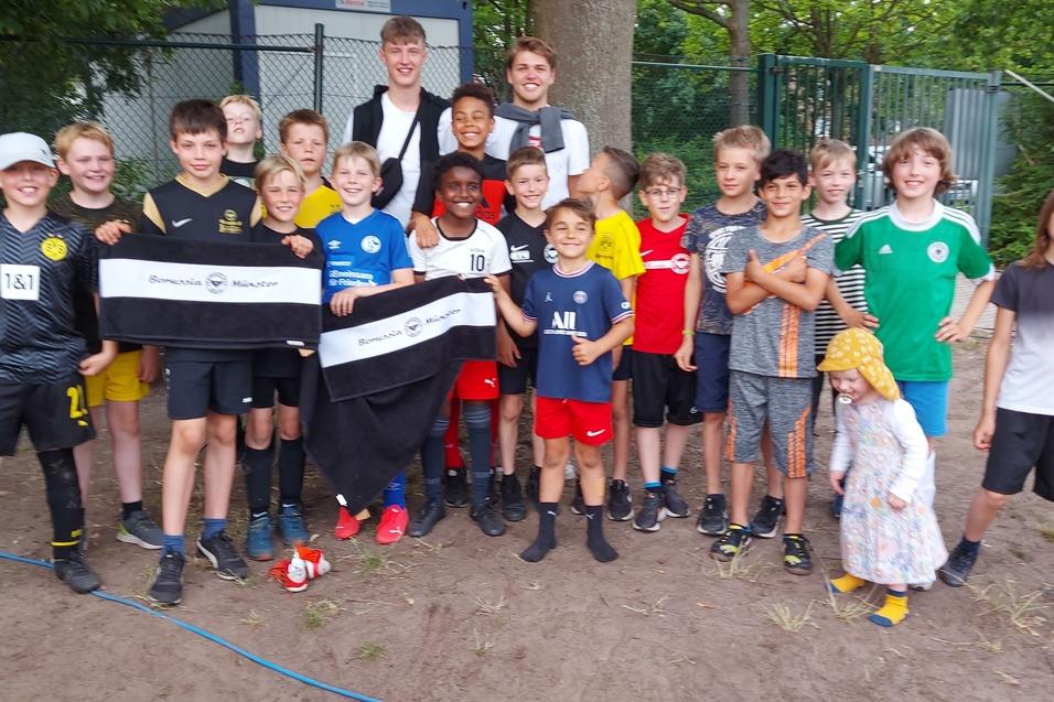 Gruppe von 18 Jungen in Fu&szlig;ballkleidung posiert zusammen im Freien, einige halten Banner.