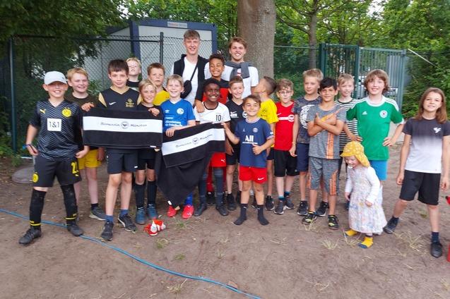 Gruppe von 18 Jungen in Fu&szlig;ballkleidung posiert zusammen im Freien, einige halten Banner.