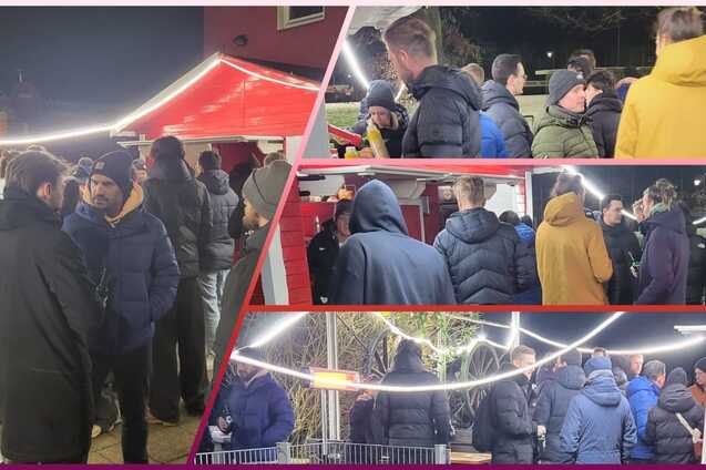 Gruppengespr&auml;ch von Menschen in warmer Kleidung an einem festlich beleuchteten Stand im Freien bei Nacht.