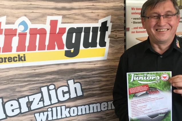 Mann h&auml;lt ein Informationsblatt vor einem plakatierten Hintergrund mit der Aufschrift &bdquo;trinkgut Gorecki&ldquo; und &bdquo;Herzlich willkommen&ldquo;.