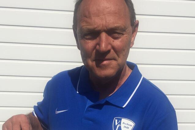 Mann in blauer Sportkleidung h&auml;lt ein Informationsblatt &uuml;ber ein Fu&szlig;ballprogramm f&uuml;r Jugendliche vor einer wei&szlig;en Wand.