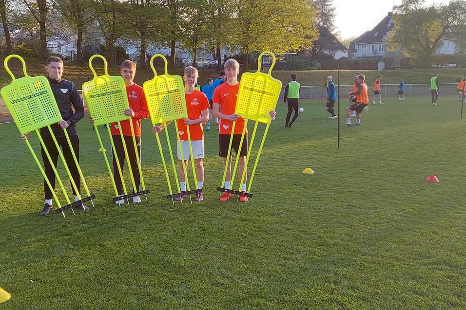 F&uuml;nf Kinder in Sportkleidung halten leuchtend gelbe Trainingspuppen auf einem Fu&szlig;ballplatz bei Sonnenuntergang.