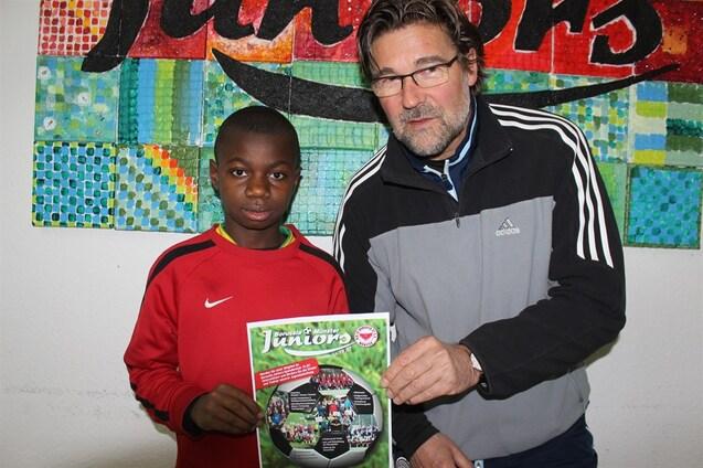 Zwei Personen stehen vor einer bunten Wand und halten ein Plakat mit Informationen &uuml;ber "Borussia M&uuml;nster Juniors."