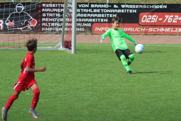 Zwei Kinder im Fu&szlig;ballspiel, ein Torwart in Gr&uuml;n f&auml;ngt einen Ball, w&auml;hrend ein Spieler in Wei&szlig; darauf zielt.