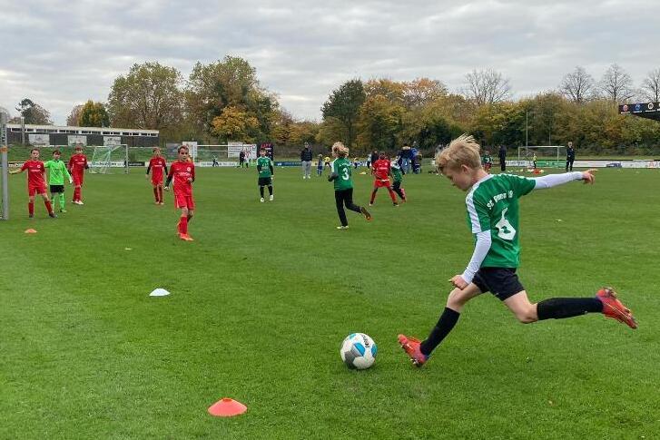 Jugendfu&szlig;ballspiel auf einer Rasenfl&auml;che mit mehrere Spielern in roten und gr&uuml;nen Trikots. Ein Spieler tritt den Ball.
