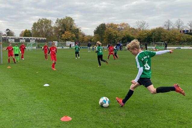 Jugendfu&szlig;ballspiel auf einer Rasenfl&auml;che mit mehrere Spielern in roten und gr&uuml;nen Trikots. Ein Spieler tritt den Ball.