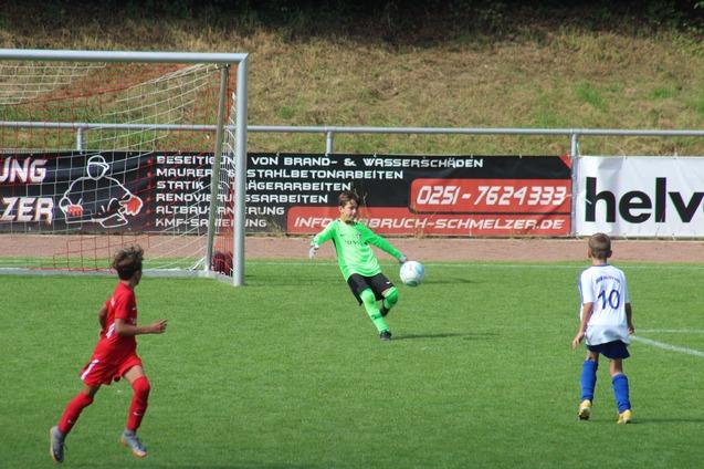 Zwei Kinder im Fu&szlig;ballspiel, ein Torwart in Gr&uuml;n f&auml;ngt einen Ball, w&auml;hrend ein Spieler in Wei&szlig; darauf zielt.