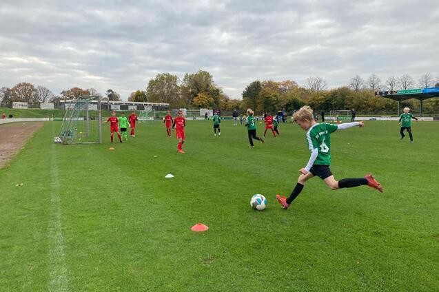 Jugendfu&szlig;ballspiel auf einer Rasenfl&auml;che mit mehrere Spielern in roten und gr&uuml;nen Trikots. Ein Spieler tritt den Ball.