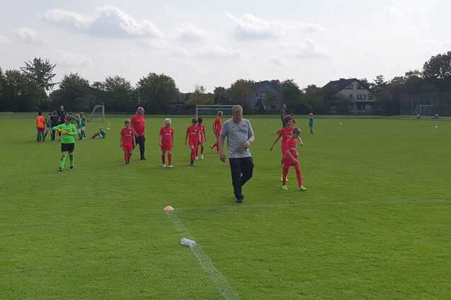 Fu&szlig;ballmannschaft in roten Trikots joggt auf einem gr&uuml;nen Spielfeld, w&auml;hrend Trainer sie anleitet.