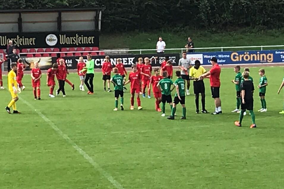 Zwei Fu&szlig;ballmannschaften in roten und gr&uuml;nen Trikots stehen auf dem Spielfeld, um an einer Besprechung teilzunehmen.