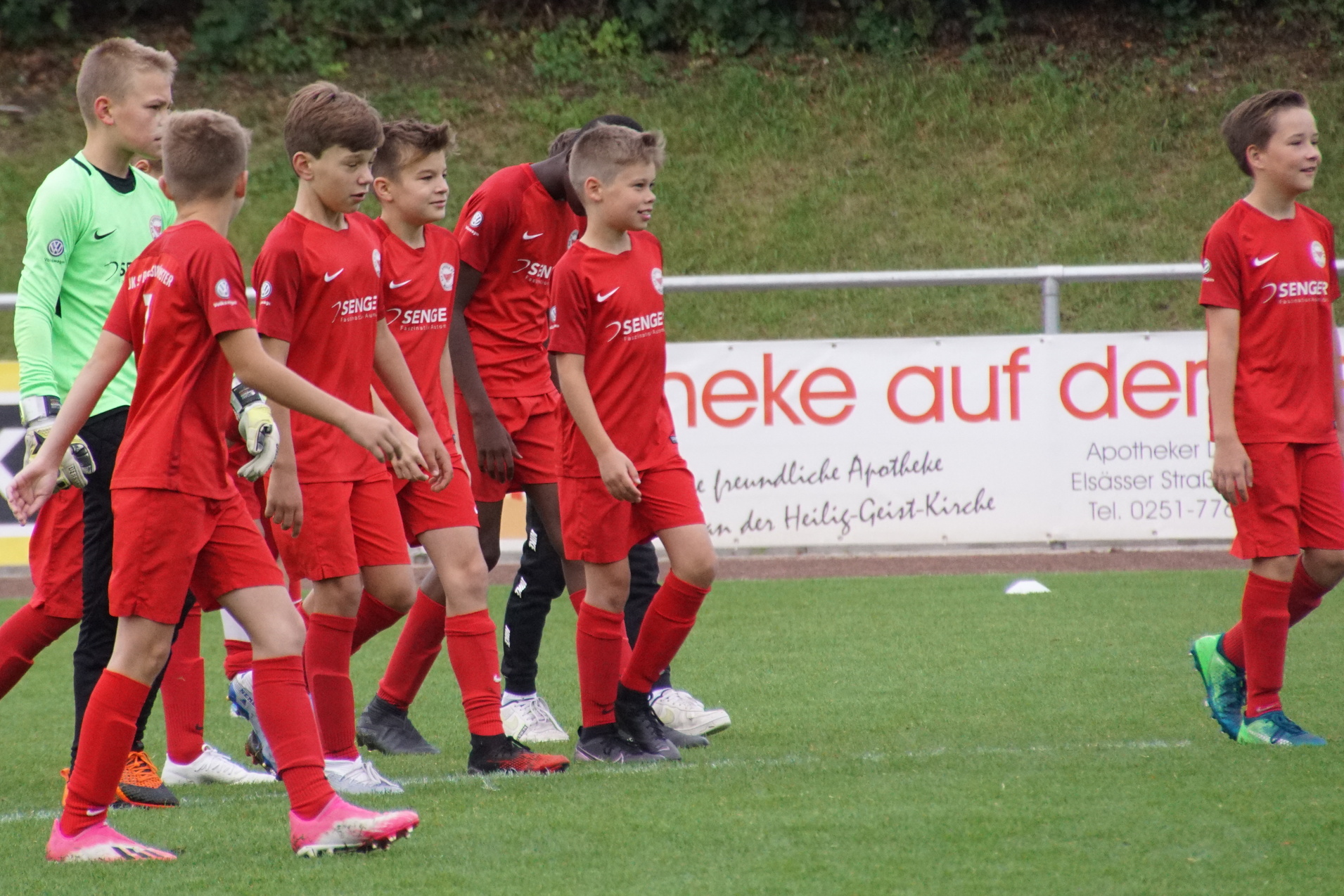 Gruppe von Nachwuchsfu&szlig;ballspielern in roten Trikots auf dem Spielfeld, ein Torwart in gr&uuml;nem Trikot dabei.