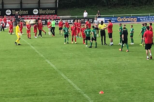 Zwei Fu&szlig;ballmannschaften in roten und gr&uuml;nen Trikots stehen auf dem Spielfeld, um an einer Besprechung teilzunehmen.