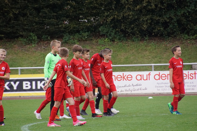 Gruppe von Nachwuchsfu&szlig;ballspielern in roten Trikots auf dem Spielfeld, ein Torwart in gr&uuml;nem Trikot dabei.