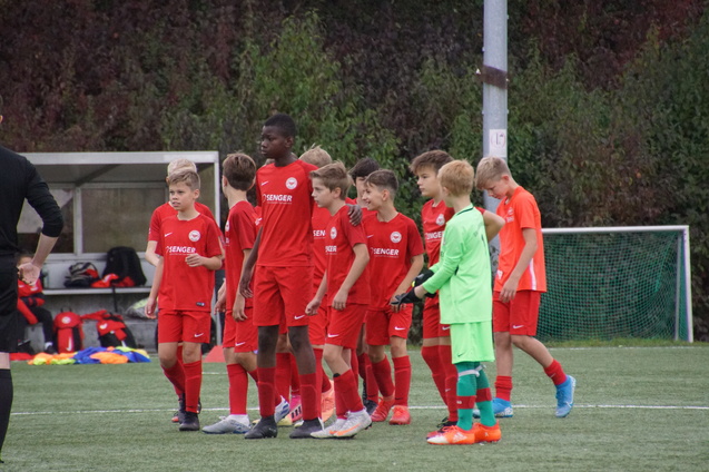 Gruppe von Jungen in roten Fu&szlig;balltrikots auf einem Spielfeld, vorbereitet auf ein Spiel, mit einem Torwart in gr&uuml;ner Ausr&uuml;stung.