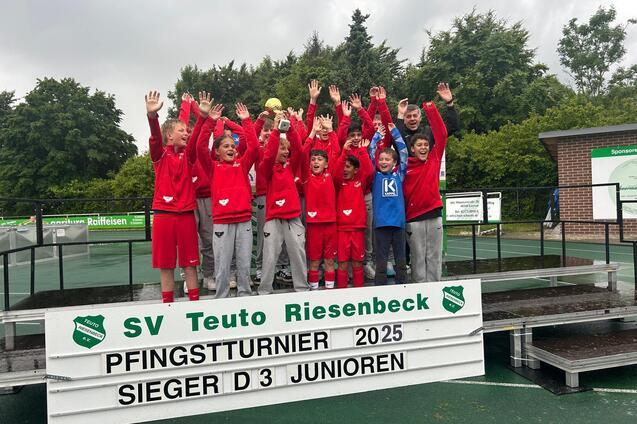 Gruppe junger Fu&szlig;ballspieler in roten Trikots feiert auf einem Siegertreppchen beim Pfingstturnier 2025.