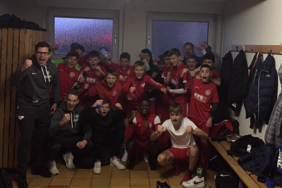 Gruppe junger Fu&szlig;ballspieler in einem Umkleidezimmer, posierend in Trikots vor B&auml;nken und Kleiderhaken.
